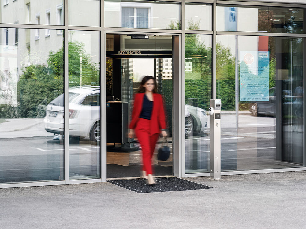 Frau im roten Kostüm gehjt durch eine automatische Schiebetüanlage