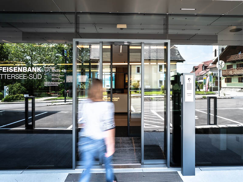 Ein Frau geht auf eine sich öffnende Schiebetüre einer Bank zu