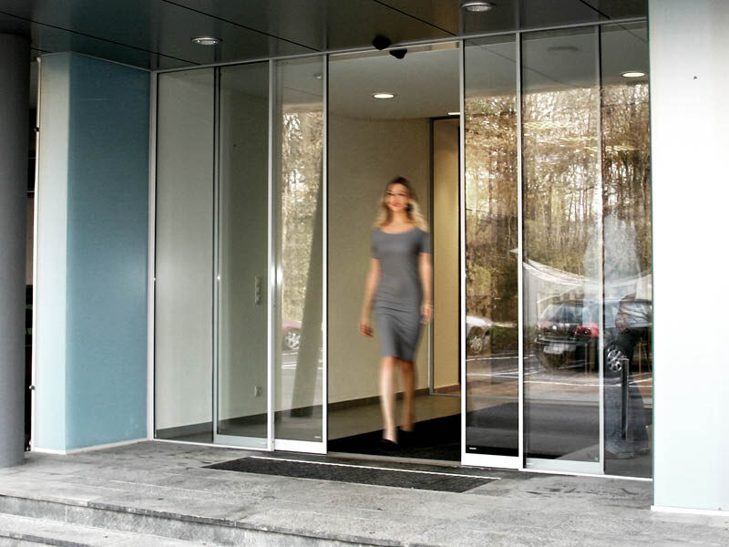 Ein Frau tritt aus einem Gebäude durch eine Automatische Schiebetür des Herstellers Symatic